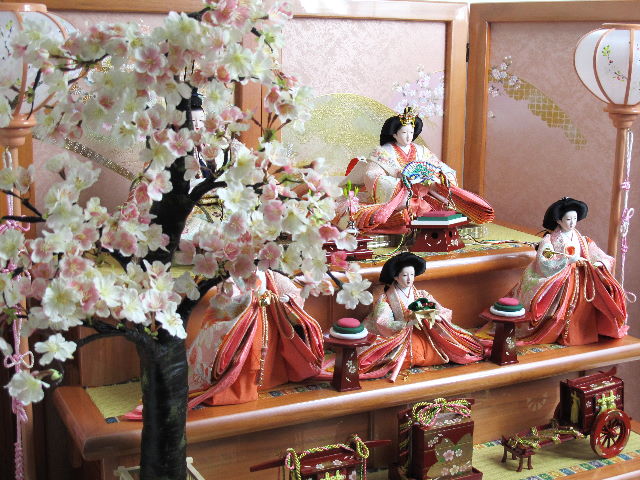 おとなしいピンクの人形をピンクの台で飾り、大きな桜を配した間口135cmの豪華でおしゃれな雛飾りです。