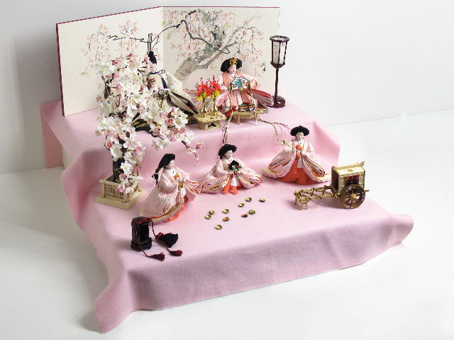 桜色のおひなさまを毛氈を敷いた二段飾りにしました。桐箱に収納します。桜の木が美しい創作雛人形です。