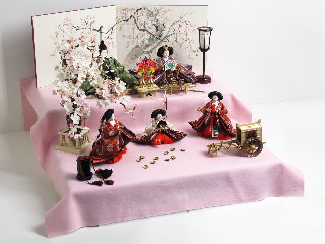 平安貴族の愛用した有職文様、鶴の丸を正絹衣装に織り込み着せ付けた、落ち着いたお雛さまを毛氈を敷いた二段飾りにしました。桐箱に収納します。桜の木が美しい創作雛人形です。