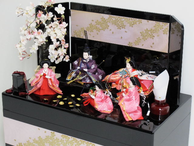 赤の女雛、濃い紫の男雛、ピンクの官女を桜吹雪をデザインした黒塗りの収納箱と組み合わせました。