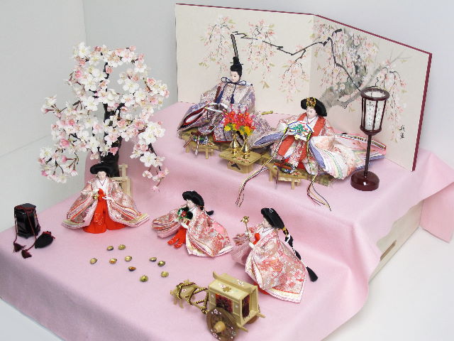 優雅な光沢で美しい赤のおひな様を毛氈を敷いた二段飾りにしました。桐箱に収納します。桜の木が美しい創作雛人形です。