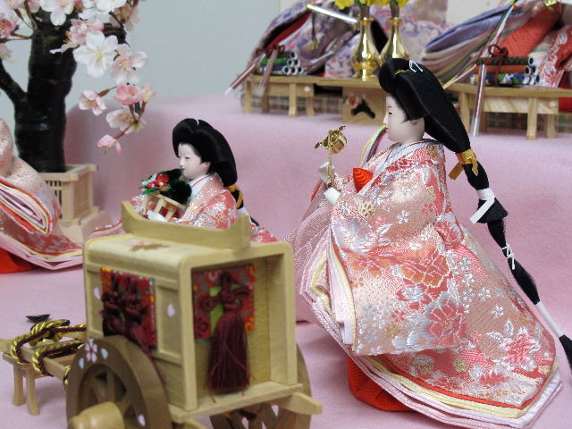 優雅な光沢で美しい赤のおひな様を毛氈を敷いた二段飾りにしました。桐箱に収納します。桜の木が美しい創作雛人形です。