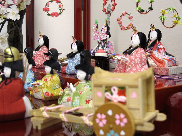 ちいさくてかわいい木目込み人形の十五人揃いです。桜柄の友禅衣装雛をため塗りの二段飾り台に所狭しと並べます。