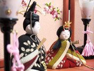 萩模様衣装の木目込み人形です。女雛が座り、男雛が立っています。桜柄の刺繍がポイントのピンク色の収納台に飾りました。
