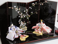 淡い桜色の女雛と藤色の男雛をシンプルに白梅の木と飾りました。重厚な溜塗り台を使用した創作親王です。