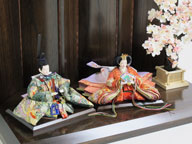 平安を意味する鳳凰を刺繍の柄とした豪華なお雛さまです。茶塗りの屏風と台に大きな桜の下を組み合わせました。